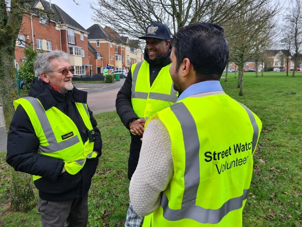 Three volunteers wearing high-vis vests stand in a semi-circle, chatting and smiling.