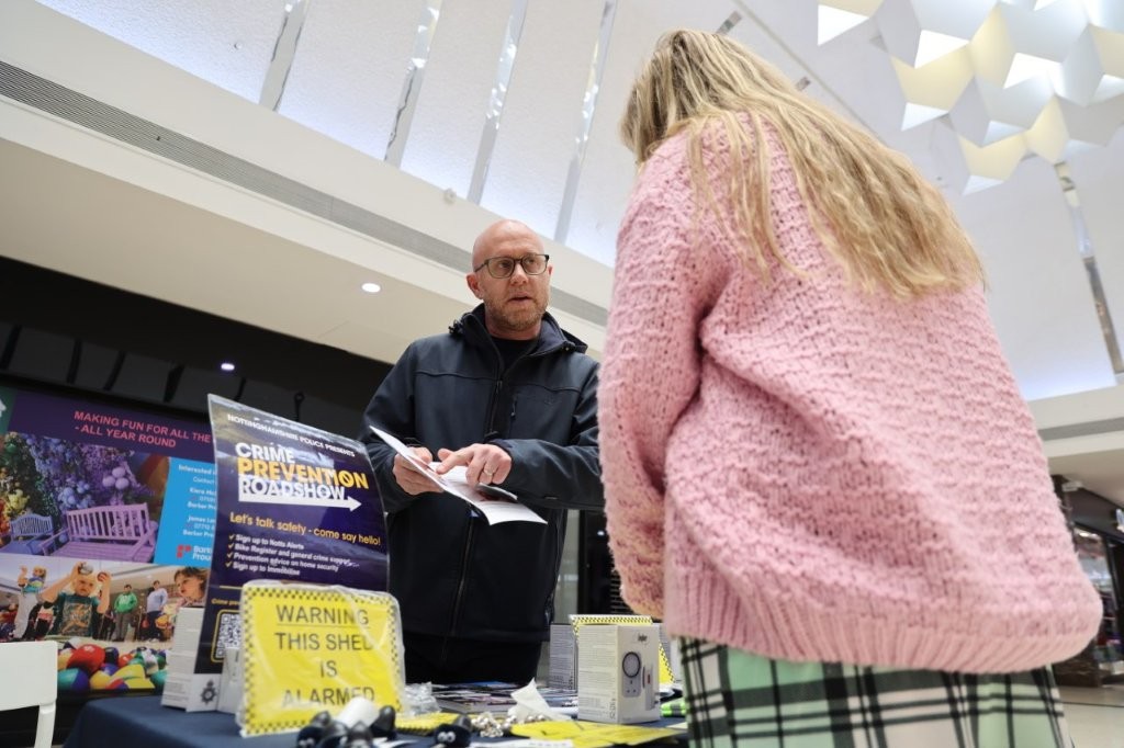 A woman stands at the roadshow table, speaking to an officer, who shows her a booklet.