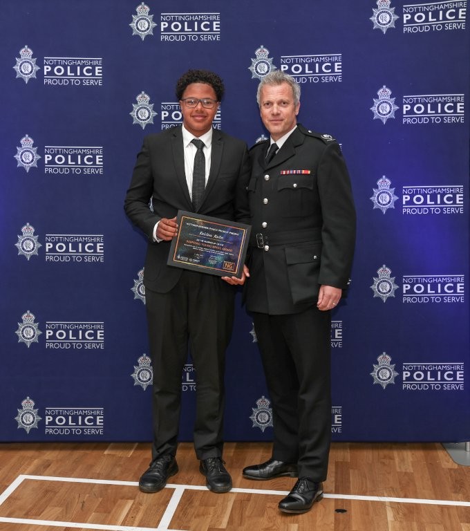 Kalilou stands in front of a police branded background with the award presenter after collecting his prizes.