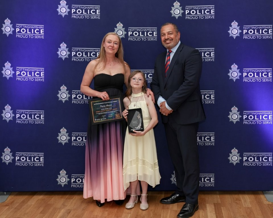 Three people pose in front of a police branded backdrop after receiving an award win.