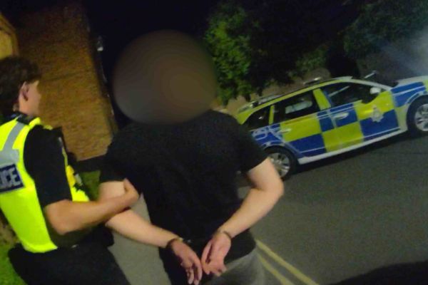 Man is led to a police car by an officer