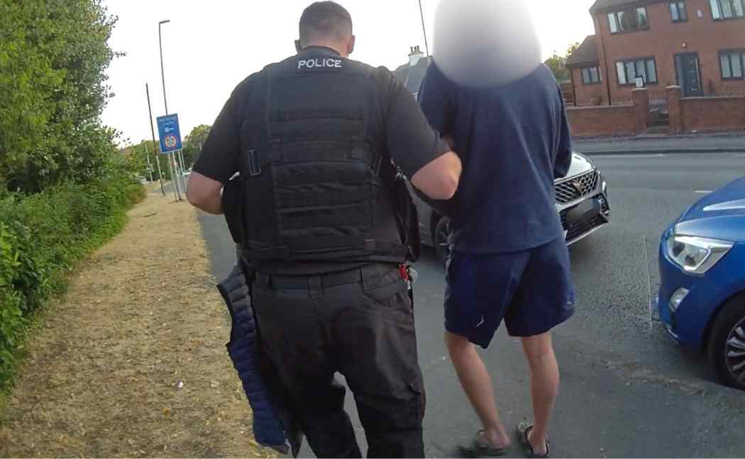 A suspect wearing Crocs is detained by an officer
