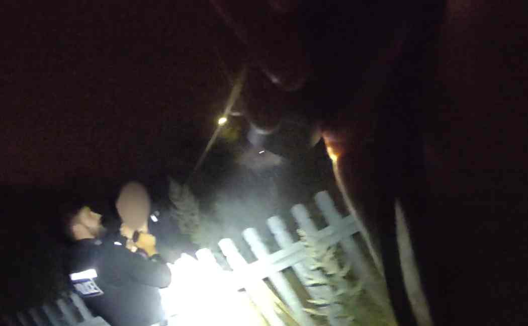 Officer shines a torch at suspect who has been detained by another officer