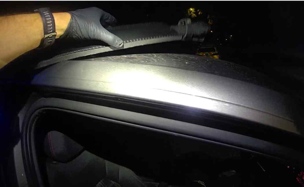 Officer holds machete in a sheath on roof of car